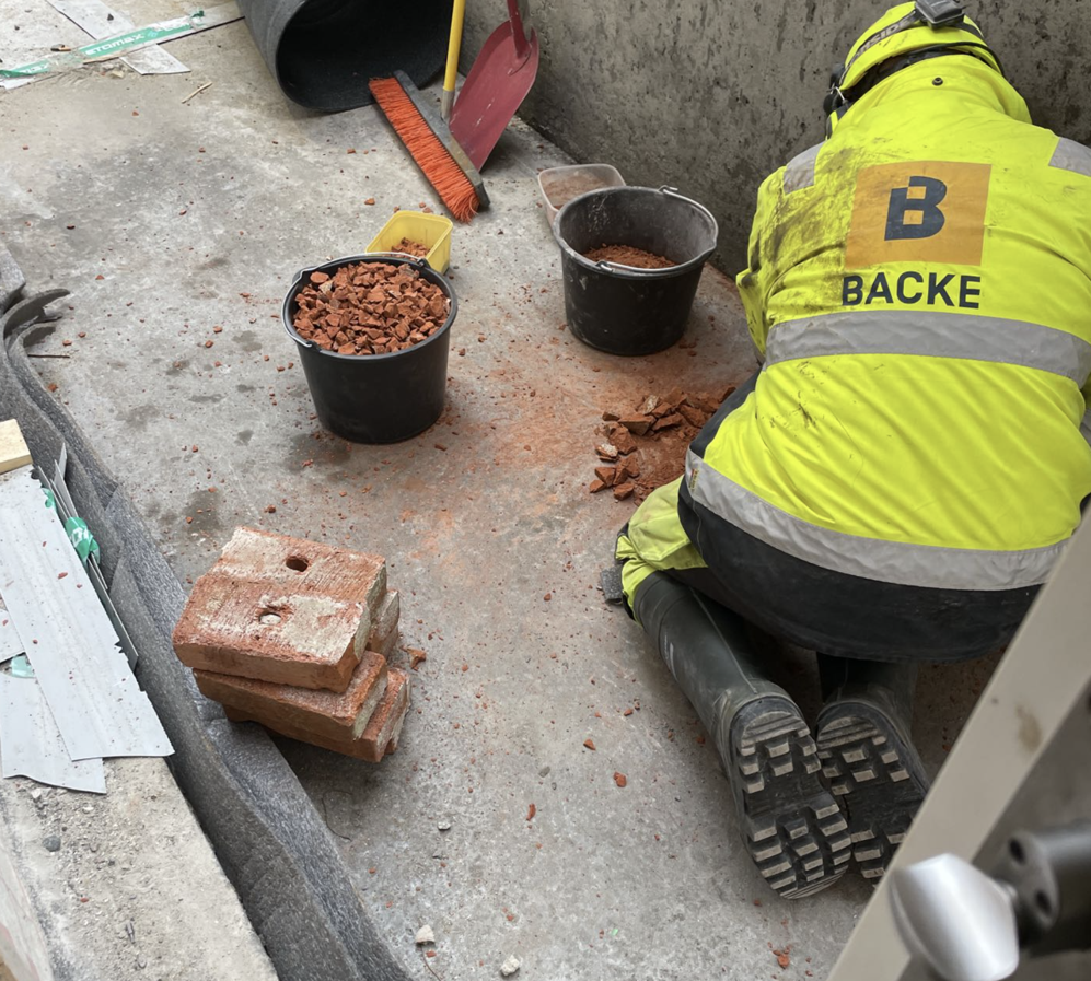 Mann sitter på knærne og jobber med å slipe betong.