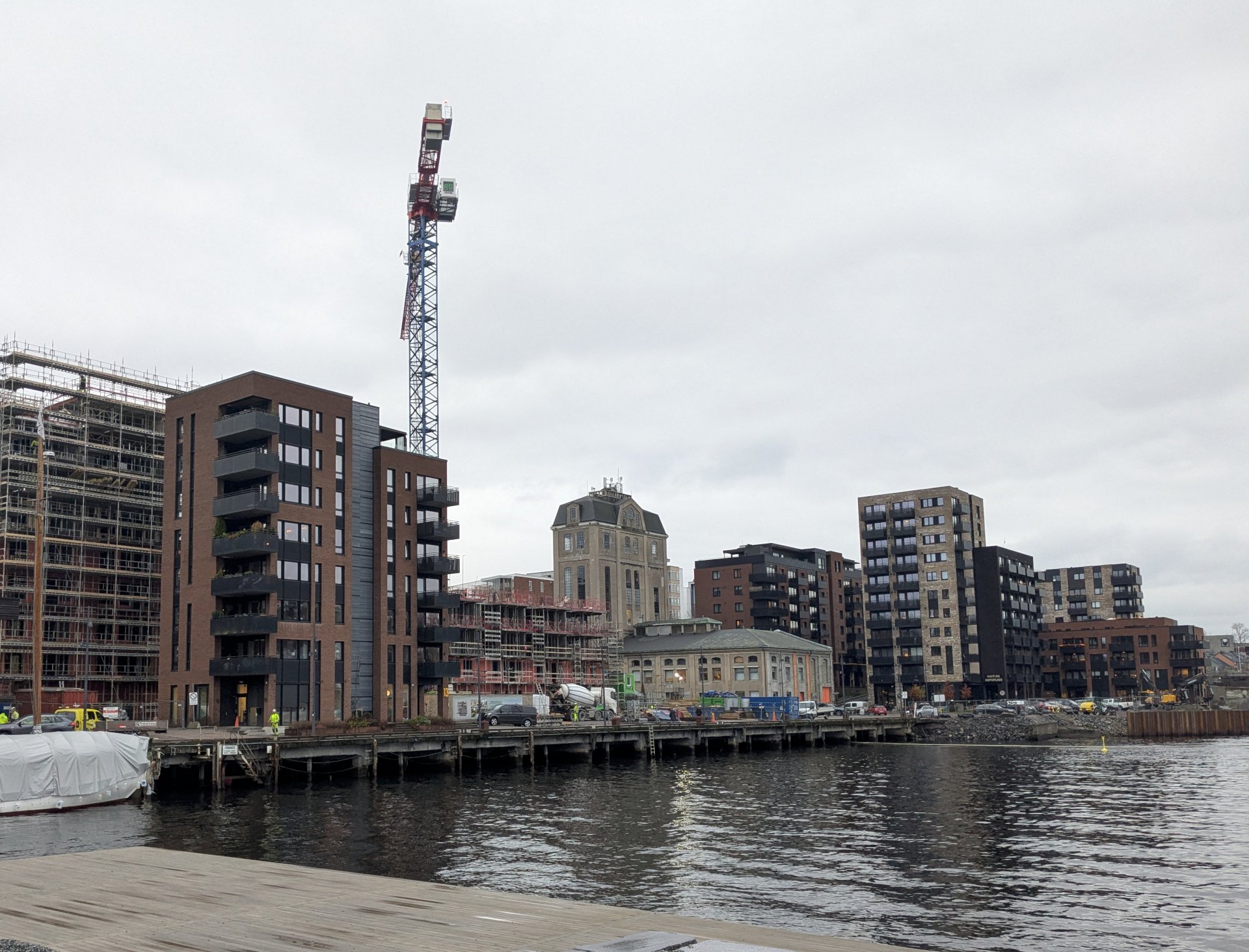 Byggeomåde langs vannet med bygg og heisekran.